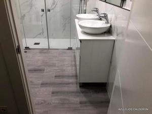 BAÑO REFORMADO. VISTA DE MAMPARA, MUEBLE CON DOS LAVABOS DE SOBRE ENCIMERA Y SUELO PORCELANICO TIPO TARIMA